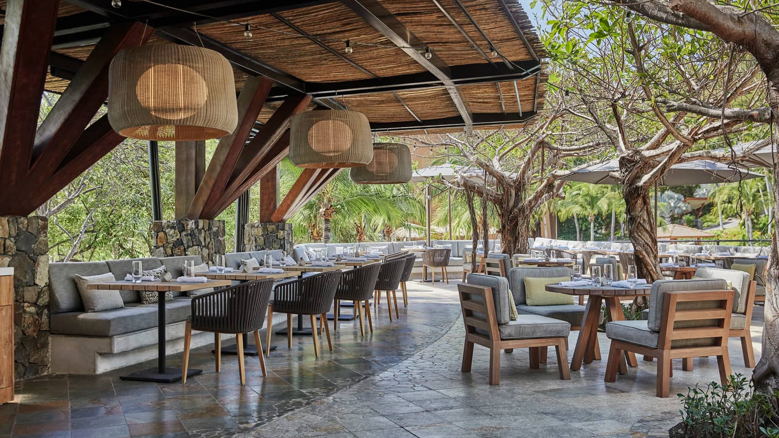 Bahia restaurant patio dining tables and chairs with thick grey cushions, large bamboo round lights hang from awning