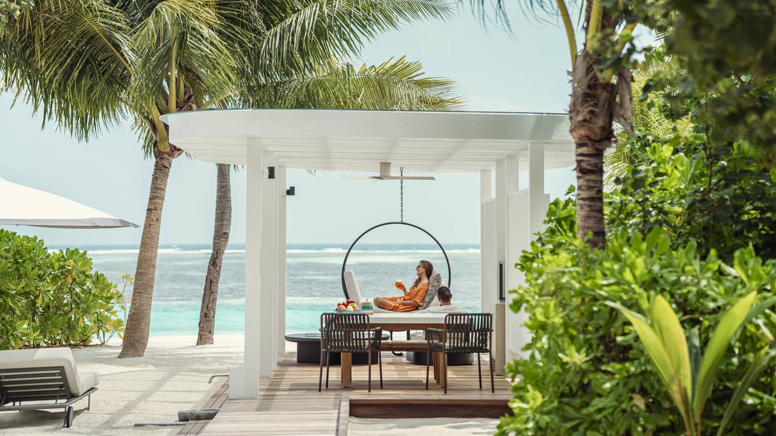 A person lounges under pergola on pool deck of private villa next to beach