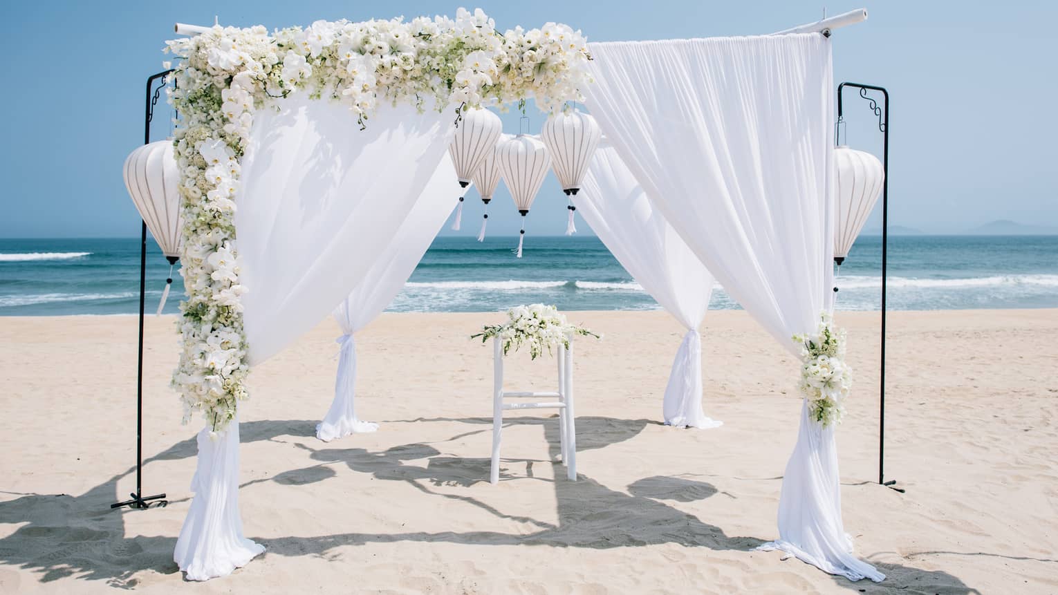 White linens and flowers draped over wedding altar on sand beach