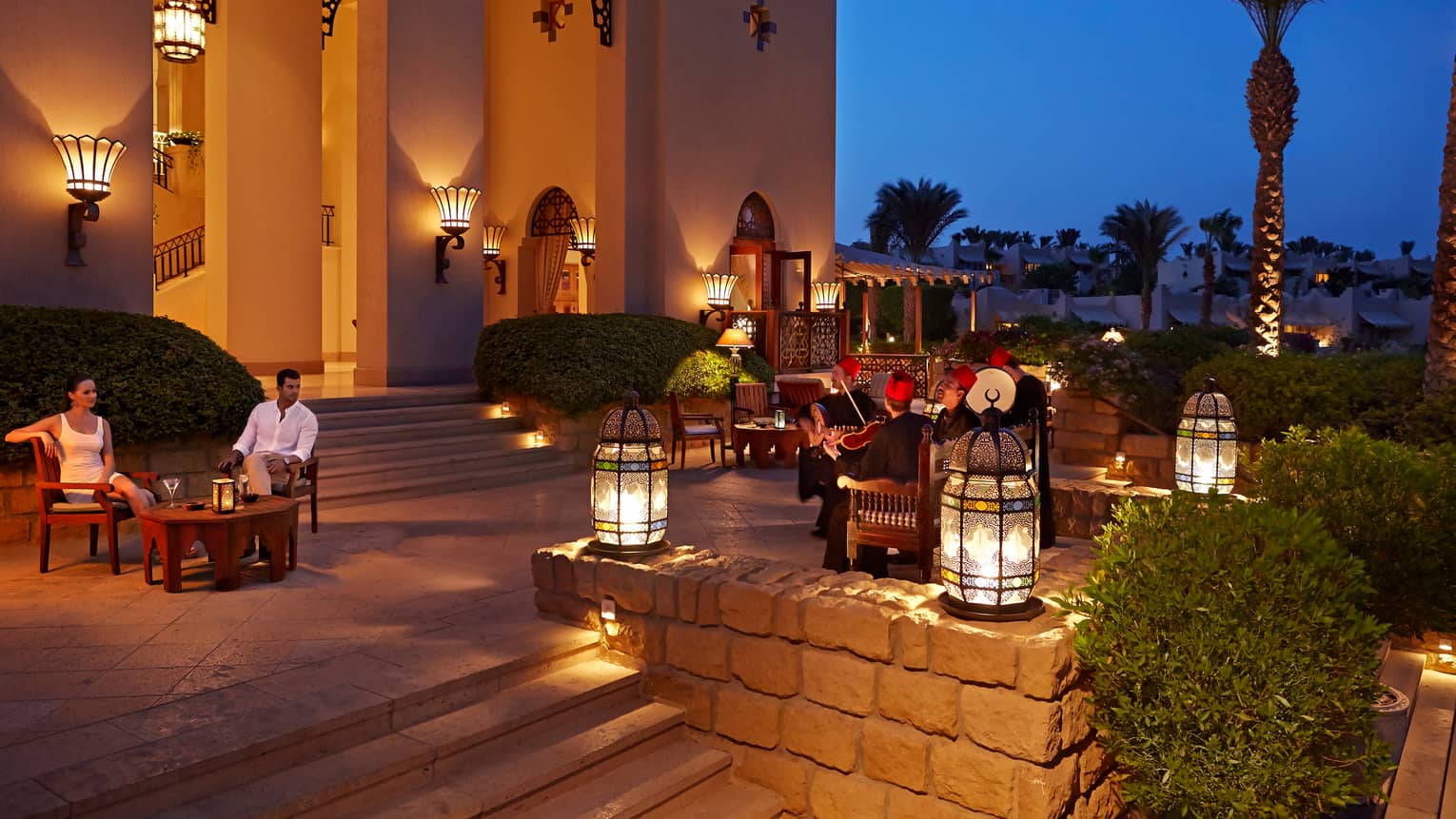 People gathered around lounge tables on outdoor patio near lanterns at night
