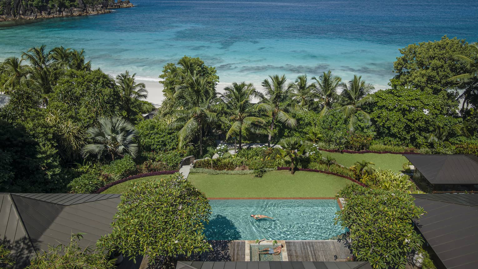 Private pool beside green lawn leading to tropical foliage and a white-sand beach and ocean beyond