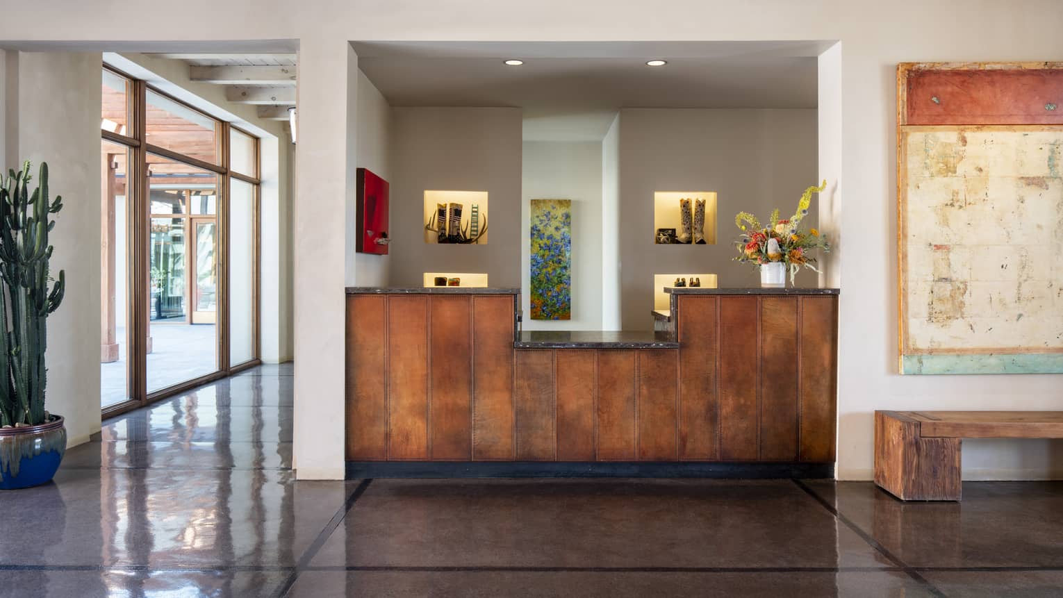A hotel lobby area with a wood front desk, cream walls and large window.