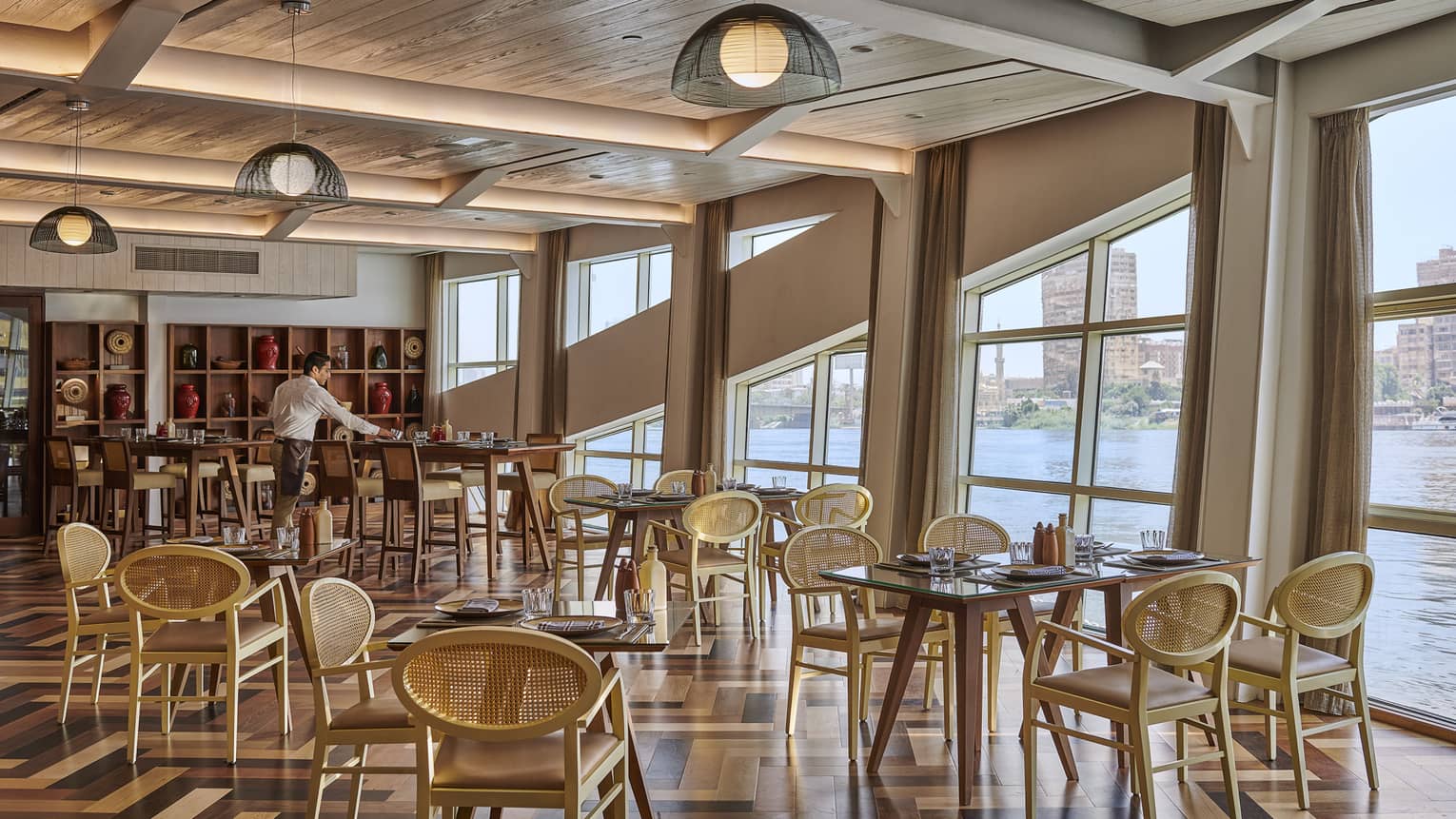 Xodó restaurant with low- and high-top tables and chairs, wooden ceiling, server, Nile view