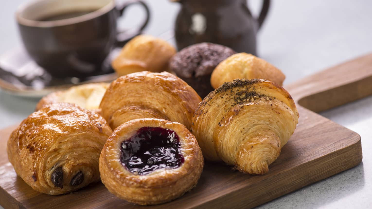Selection of pastries on a board with a cup of coffee and pitcher of cream in background