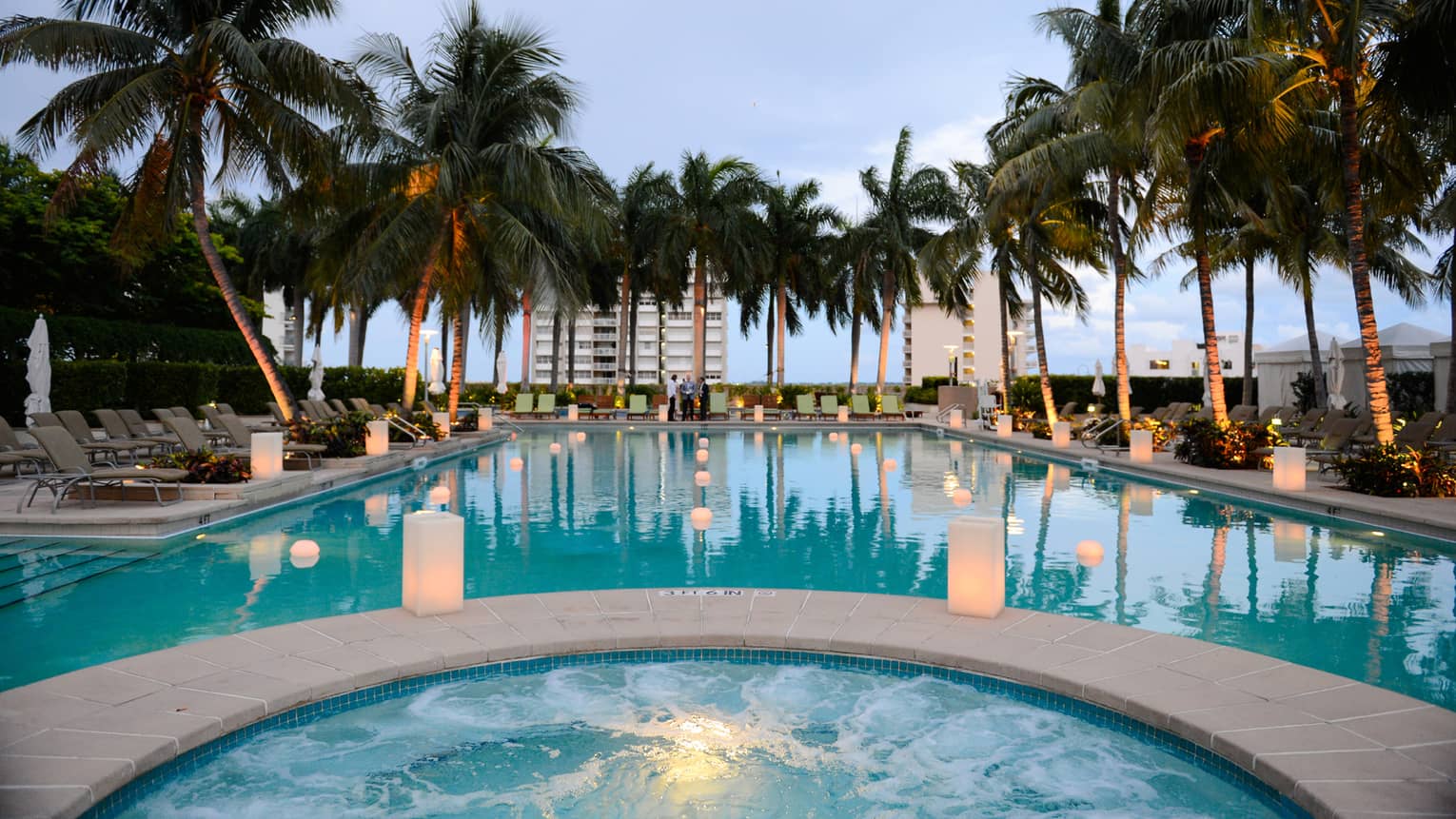 White lanterns glow along outdoor pool lined with palm trees
