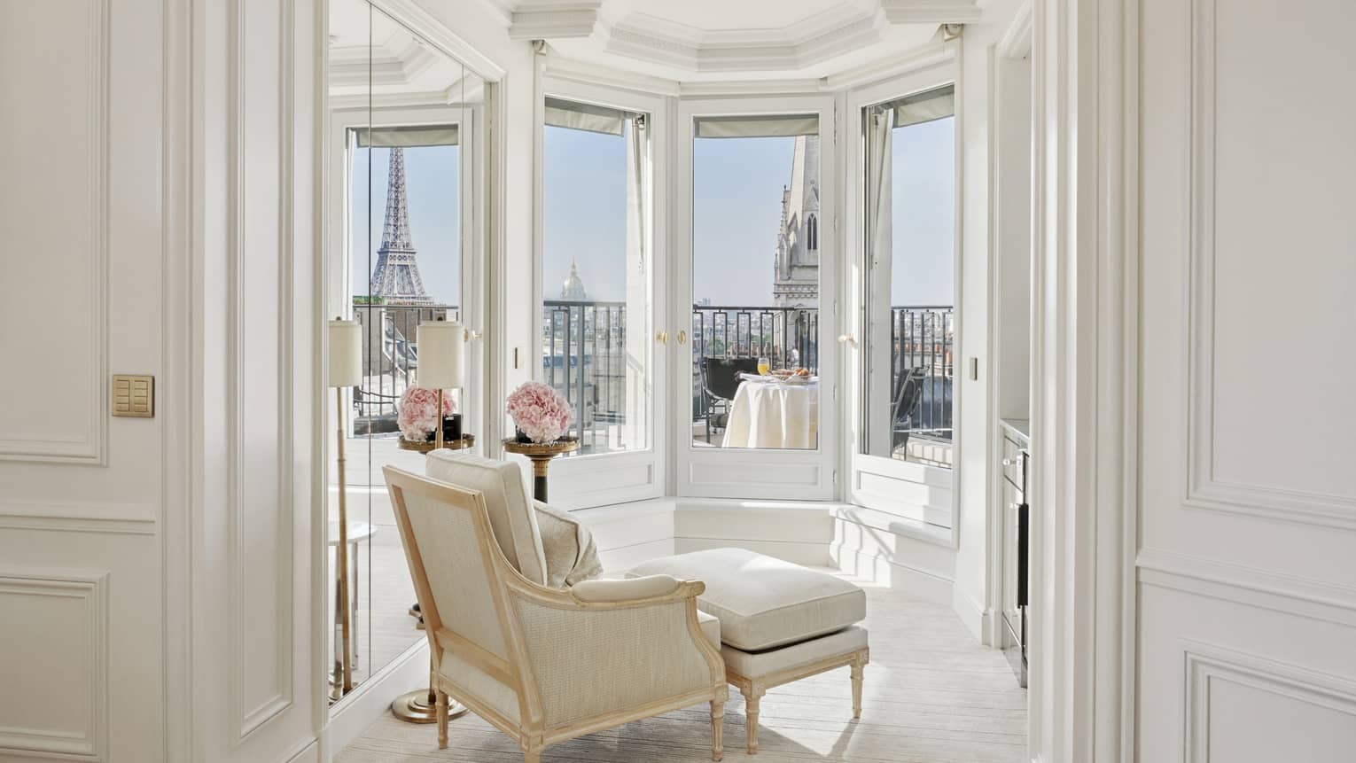 A white room has windows and a balcony with a direct view of the Eiffel Tower