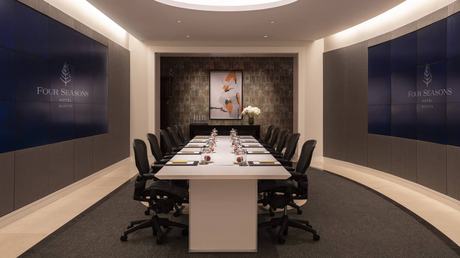 A meeting room with a large white boardroom table surrounded by black chairs with wheels.