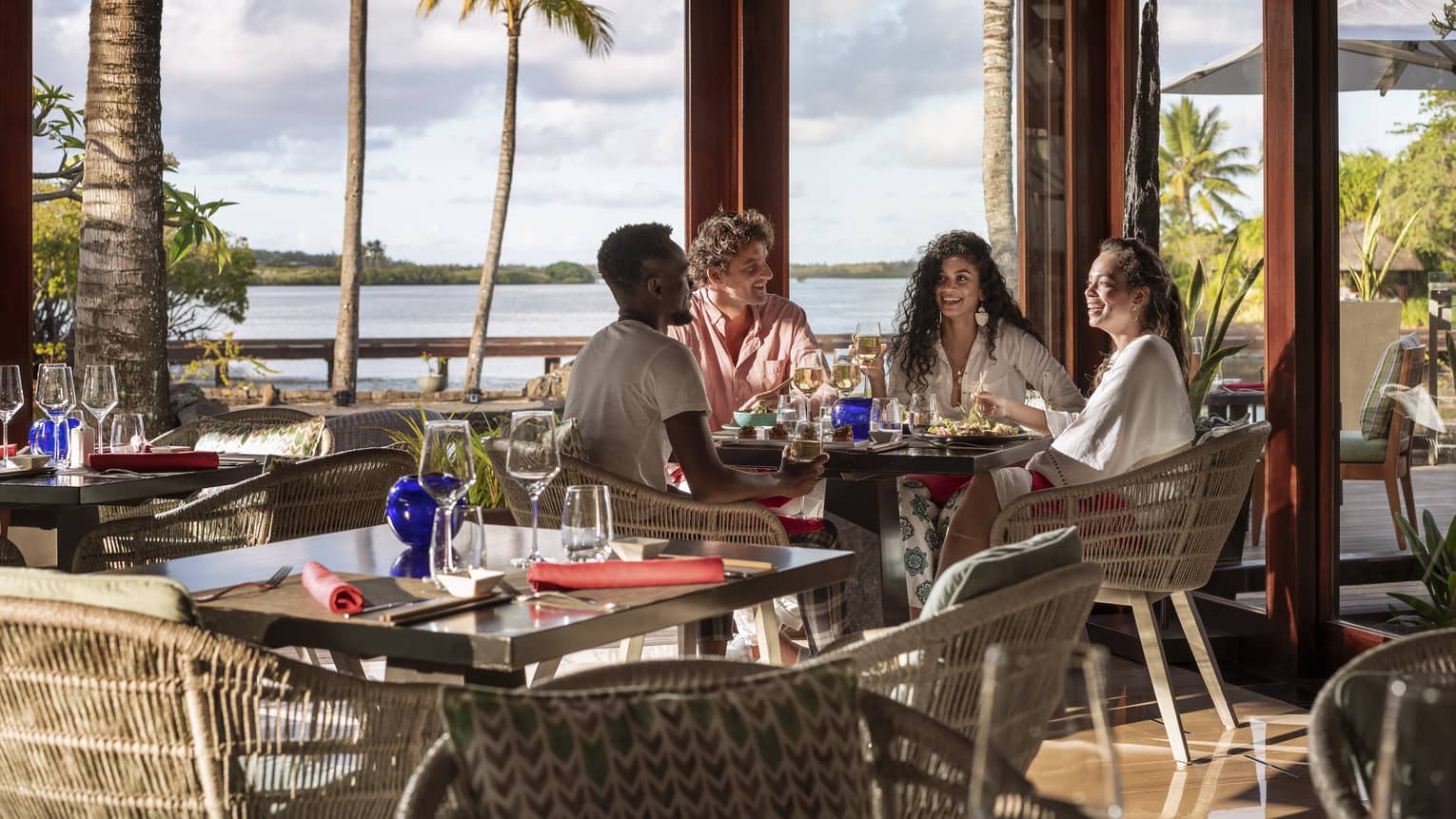 Four friends sitting and talking over food and wine at waterfront restaurant with tall windows