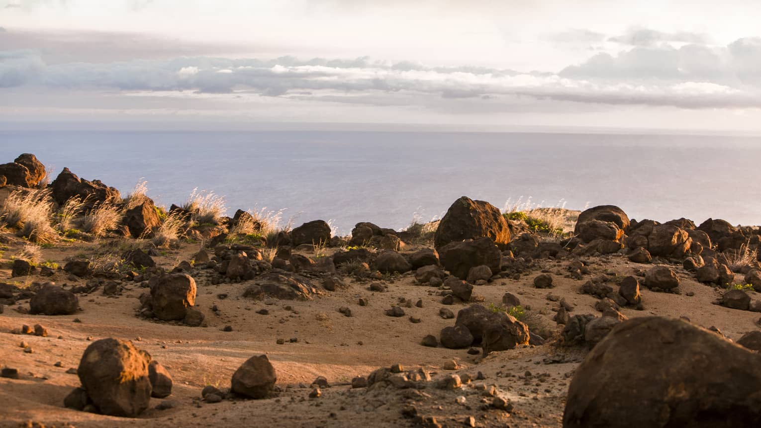 Rocky cliffside at sunset overlooking the ocean, wispy white clouds above