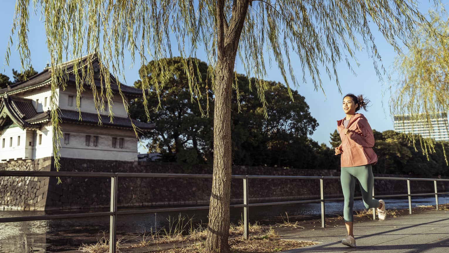 Woman jogs by Japanese temple and moat