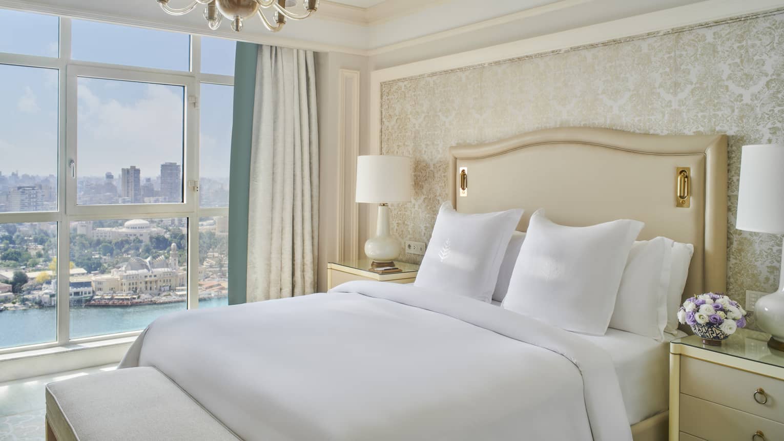 Guest bedroom with king bed, white linens and cream tufted headboard; floor-to-ceiling window with views of the River Nile