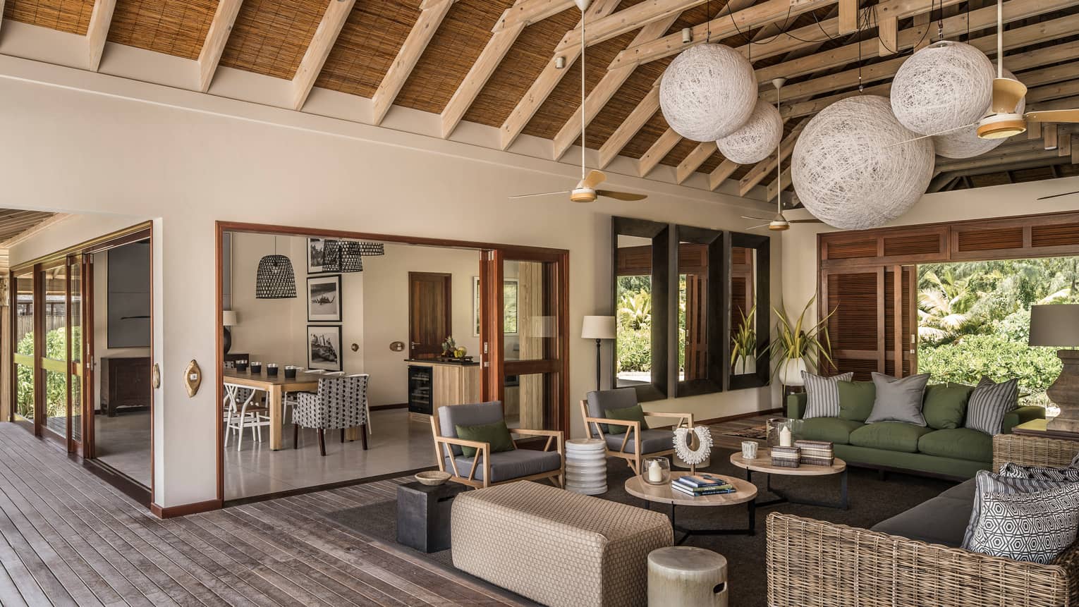 Large wicker globe chandeliers hang from beamed roof over open-air living room