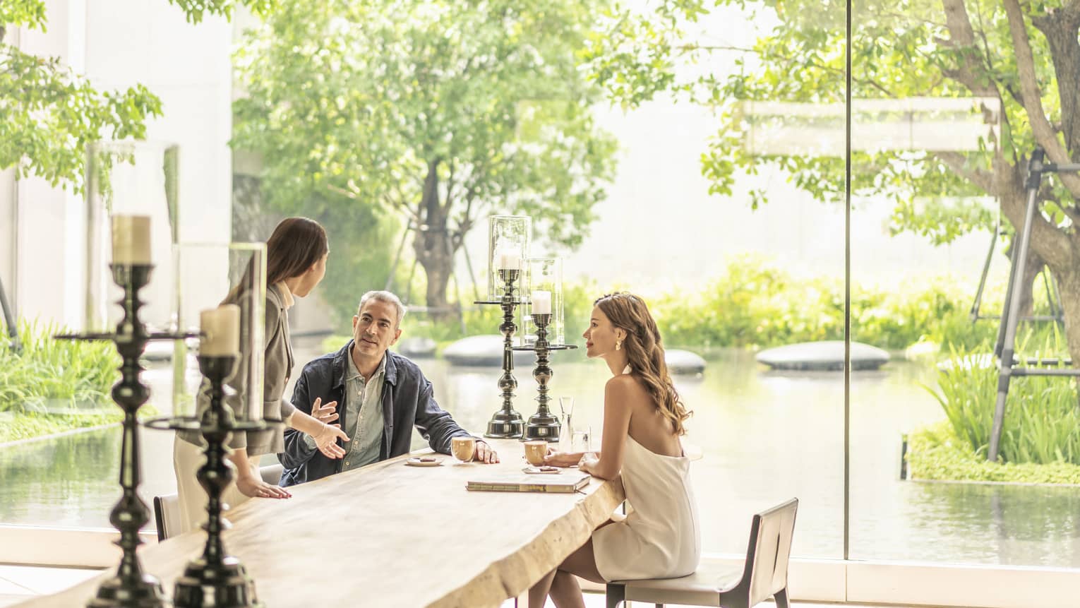 Couple chats with staff member at table at The Lounge, pond views