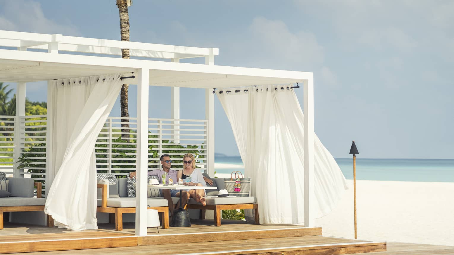 Guests enjoying cocktails and a slight breeze next to the water at a Blu Beach Club Cabana
