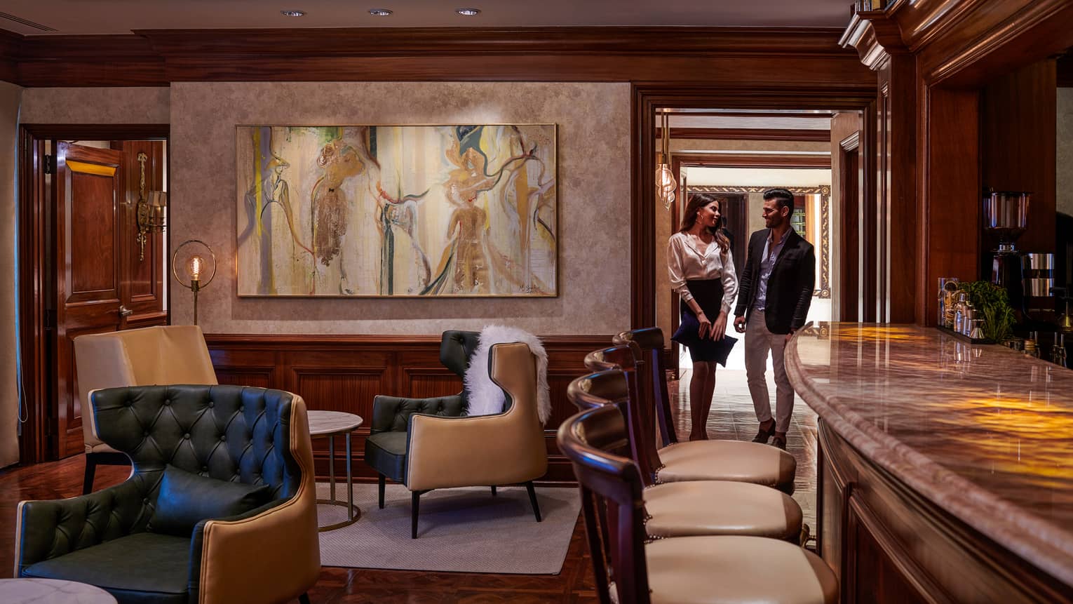 Woman and man walk through door into cocktail lounge with large painting, leather chairs
