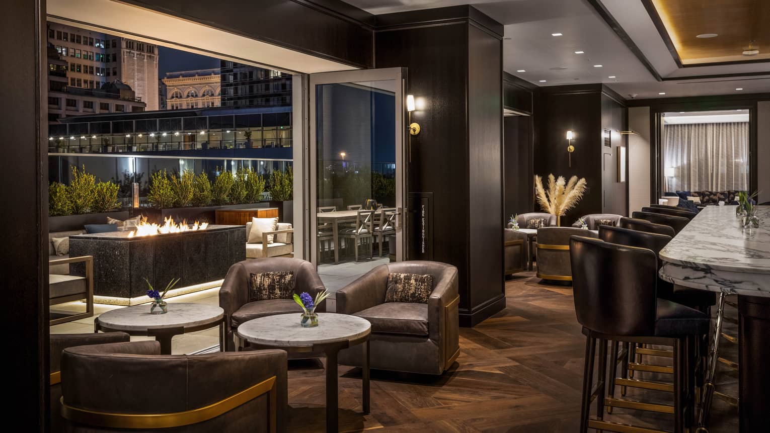 Bar area with fireplace, lounge chairs and view of the city through large windows.