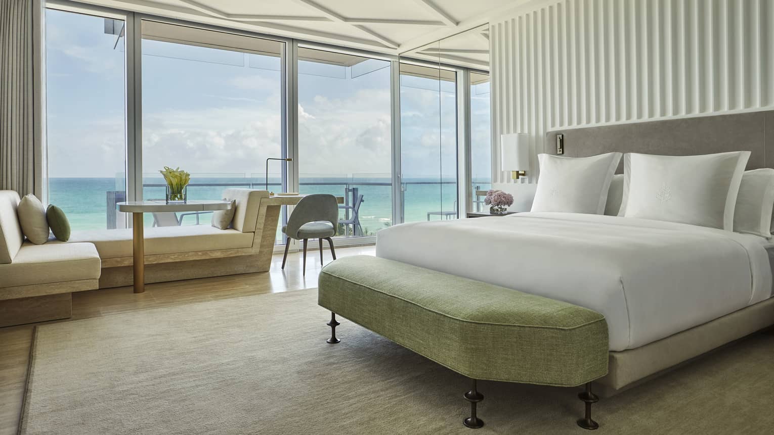 Luxurious beachside suite with white wedding, sofa, floor-to-ceiling windows overlooking patio and ocean views