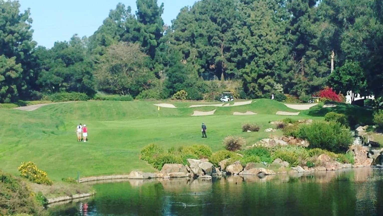 View of golfers on green from across pond on sunny day