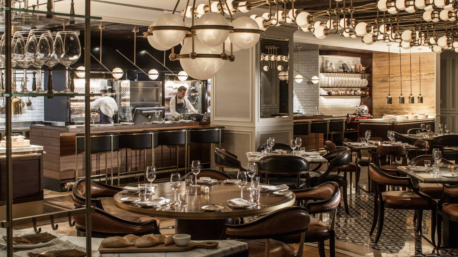 La Capitale dining room with dark, wood decor, round tables and chandeliers, globe chandeliers, chefs in open kitchen