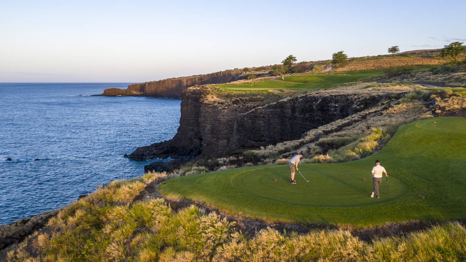 Two golfers at the 12th-hole tee at Manele Golf Course at Four Seasons Resort Lanai, cliffs and ocean in background
