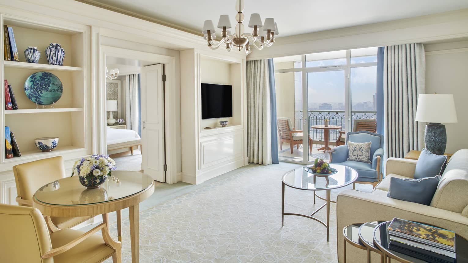 Premium Executive Suite living area with cream couch and blue accent pillows, blue armchair, sliding glass door to balcony, doorway to bedroom