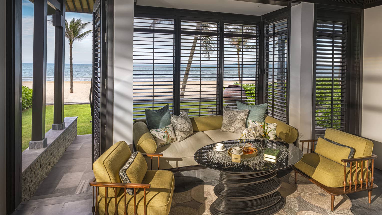 Guest room living area with mustard-coloured arm chairs, round coffee table and floor-to-ceiling windows with beach views