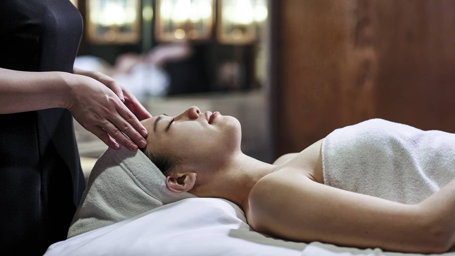 Woman getting a head massage during spa treatment, white towel over her and her head