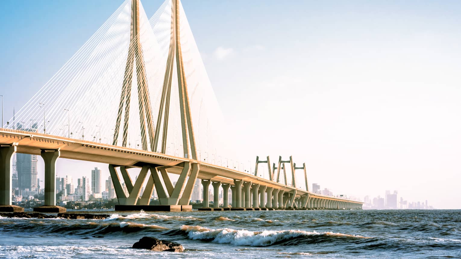 View from the water of a kilometres-long bridge featuring a triangular tower connected by scores of luminous steel cables.