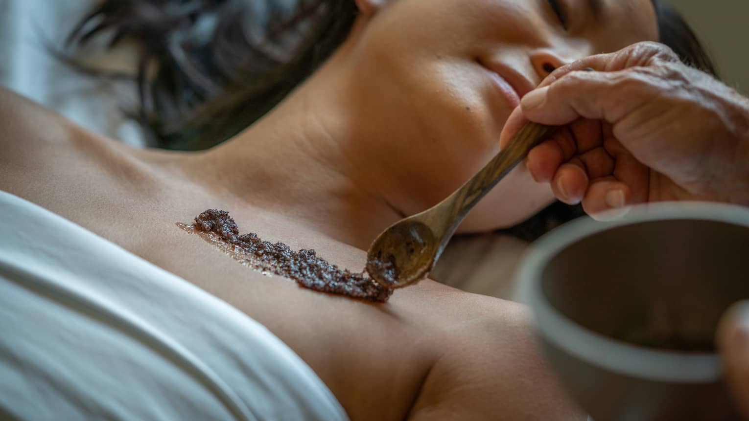 Person laying on a Spa bed while an exfoliating skin scrub is placed on their skin.