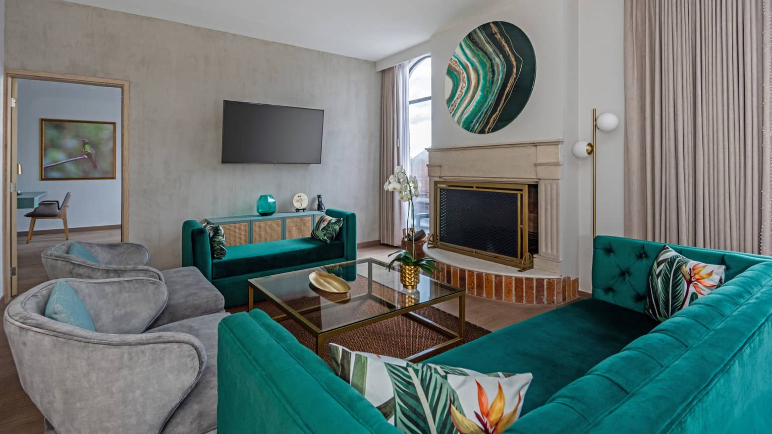 Kelly green couch with accent pillows, two grey accent chairs, glass coffee table, fireplace, doorway to bedroom