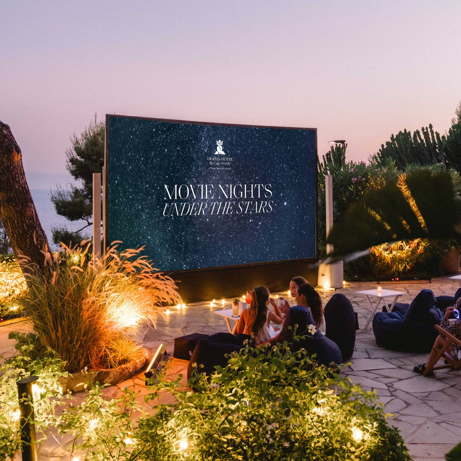 Families sit in front of a large outdoor movie screen