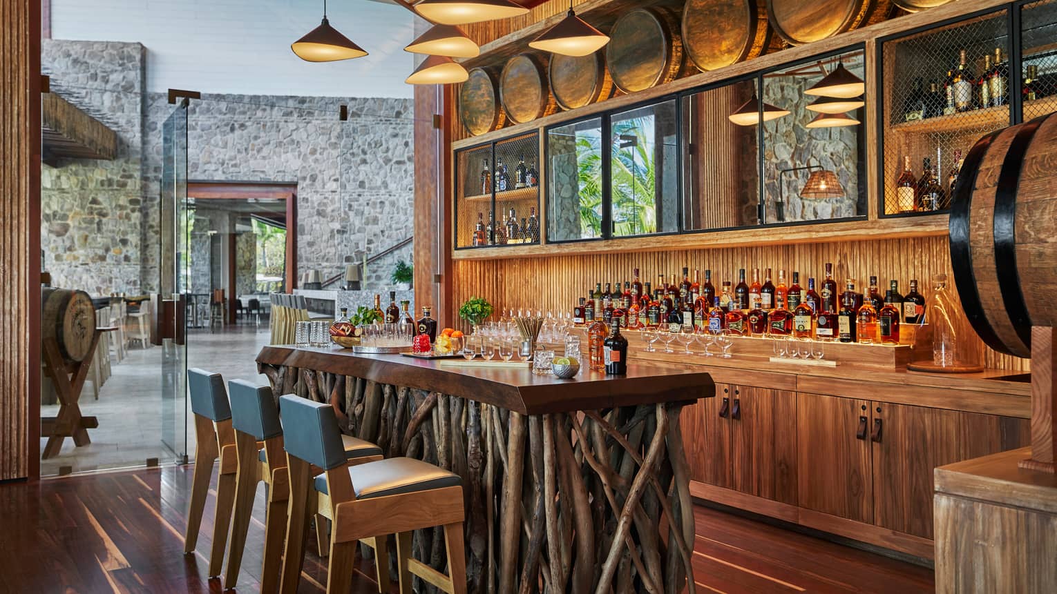 Modern chandelier above rustic wood tasting bar made from sticks, blue chairs, liquor display, barrel