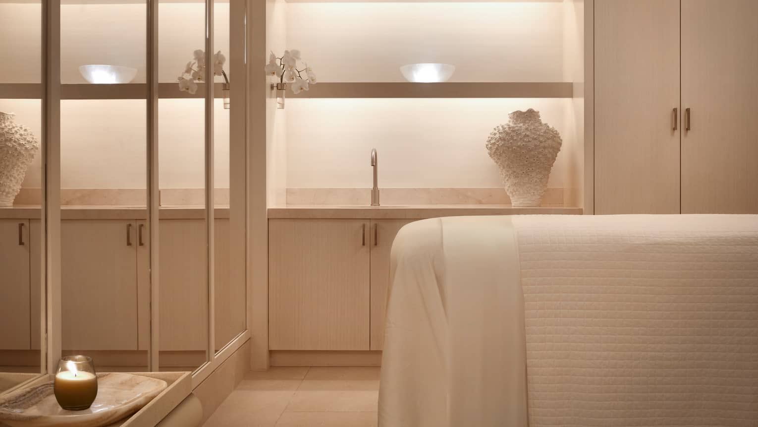 Spa treatment room bed with white linens across from mirror wall