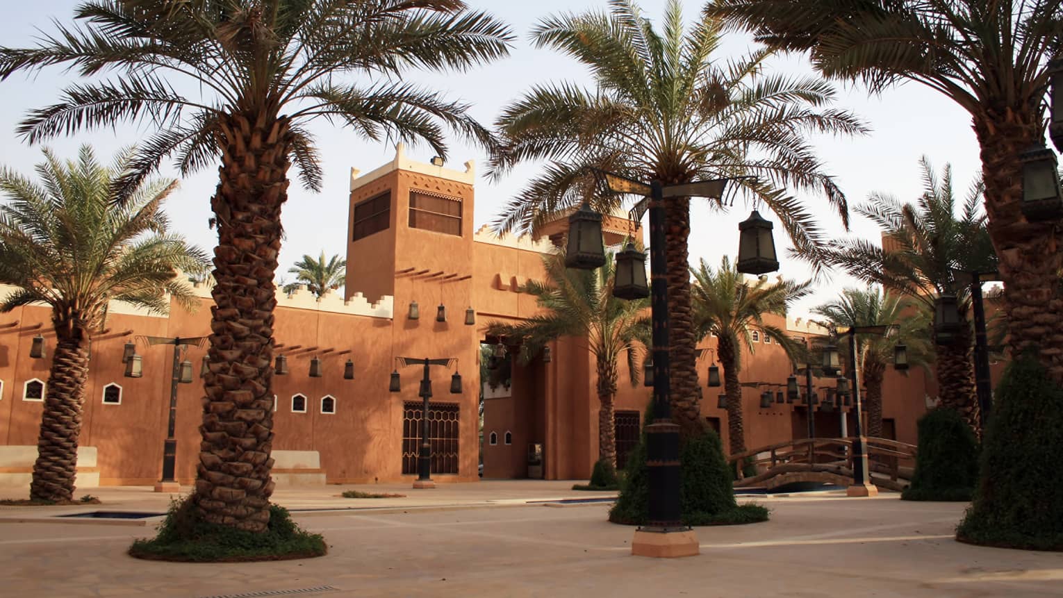 Sunny exterior of sandstone building and large palm trees with lanterns hanging from branches