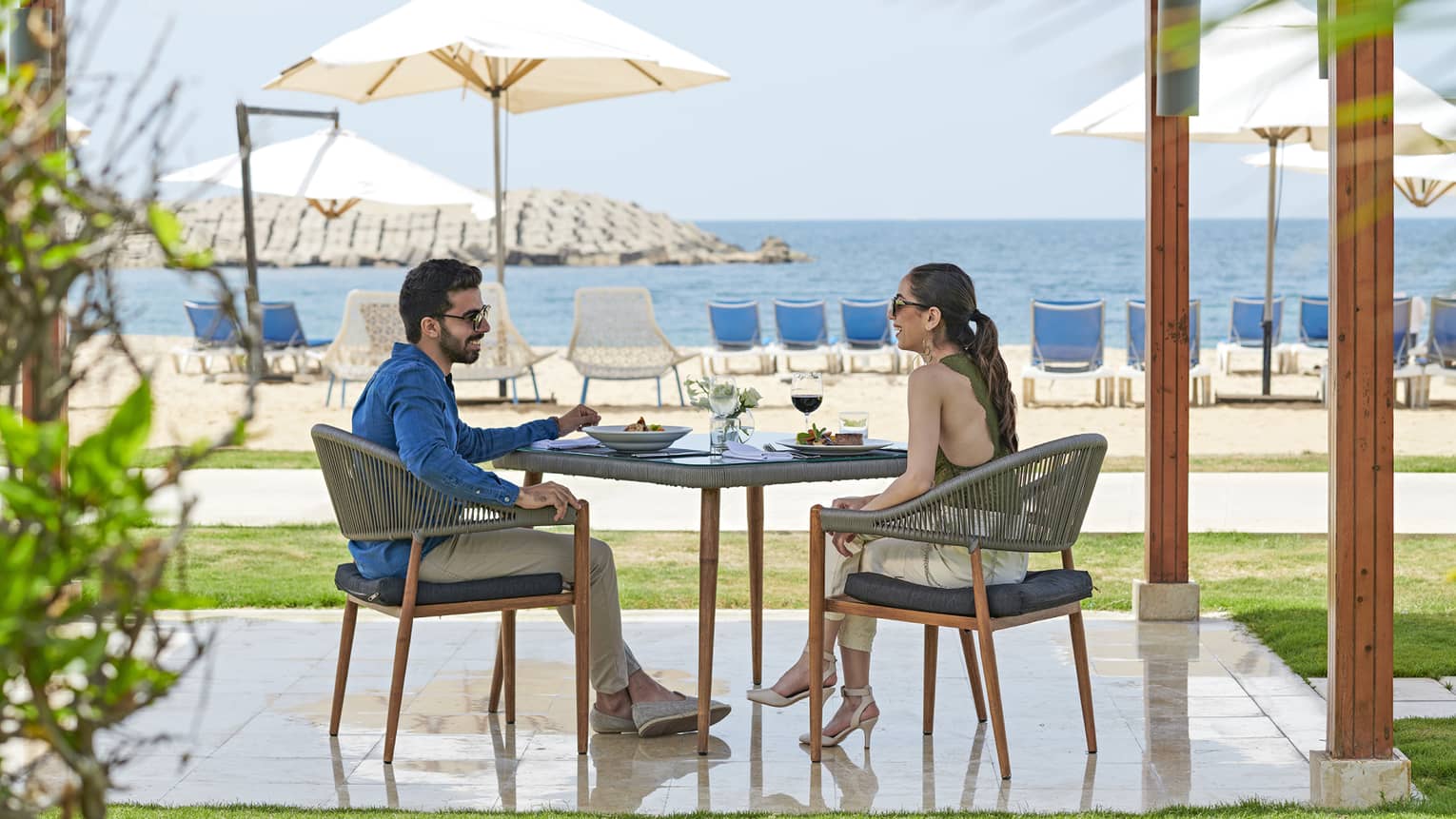 Smiling couple dines at patio table on private pergola near white sand beach