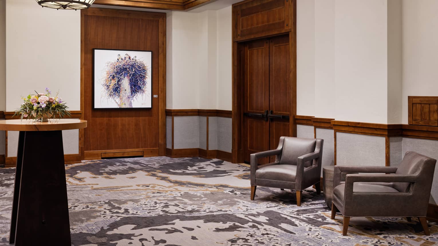 The corner of a room with two chairs, art on the wall and a standing table.
