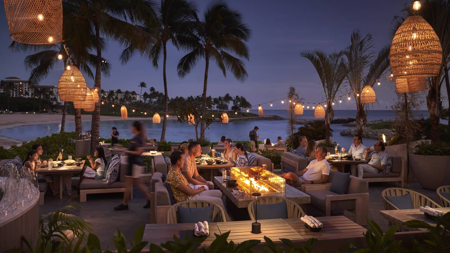 Guests dining at dusk on lagoon-side restaurant patio draped in lanterns