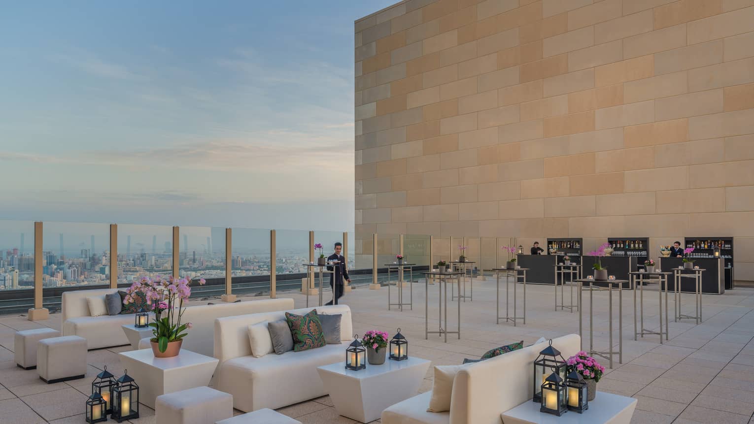 White sofas, lanterns on rooftop function space by tall brick wall