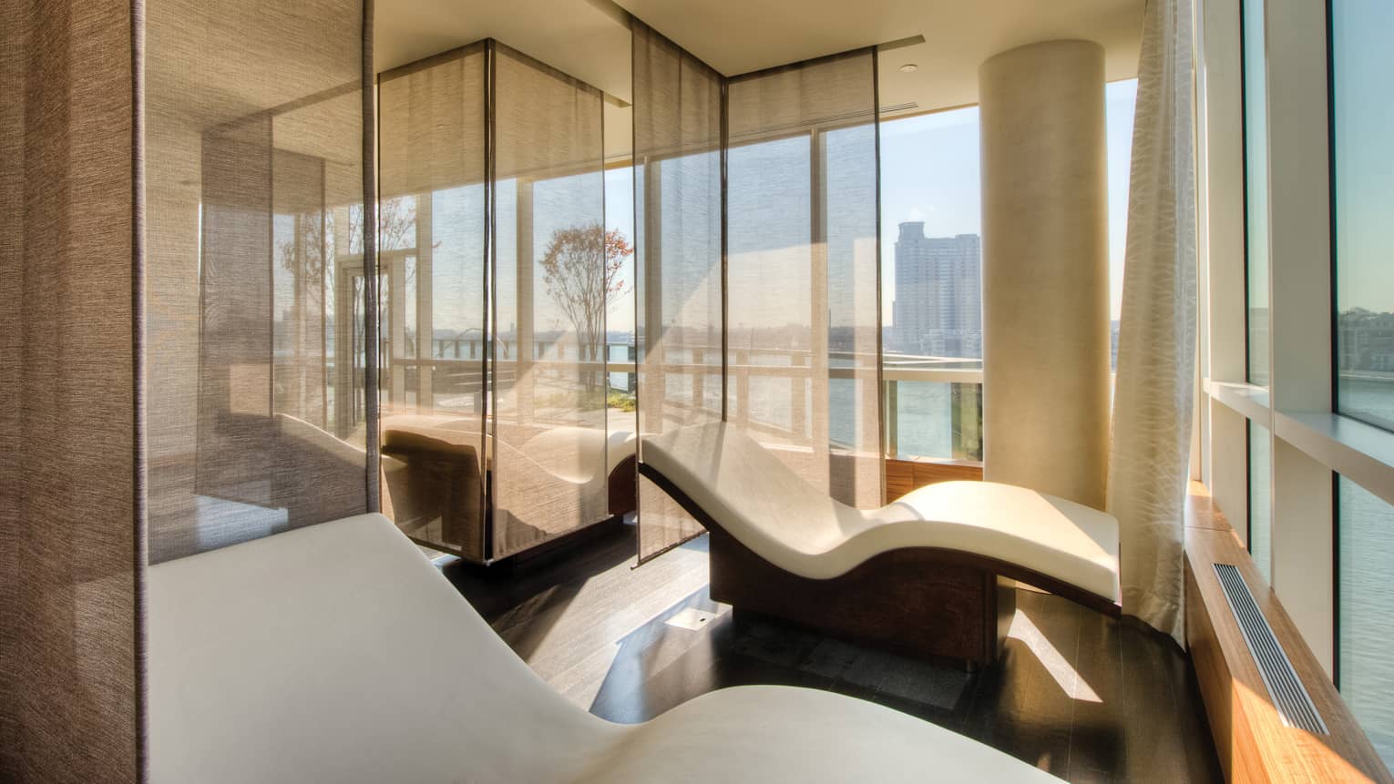 Curved white spa chairs divided by sheer panel curtains in spa