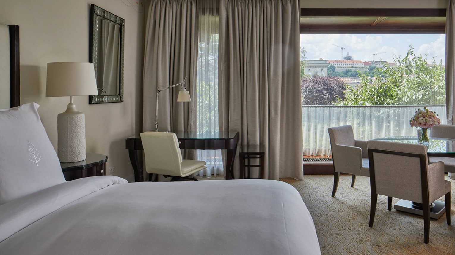 A room with a bed, desk and chair, table and chairs and large window.