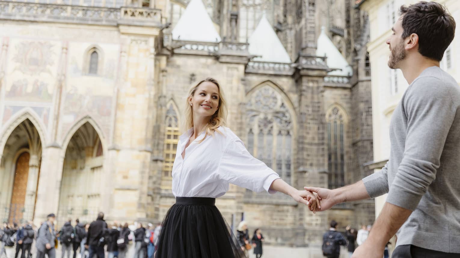 Couple smiling, holding hands with arms stretched as they tour historic city