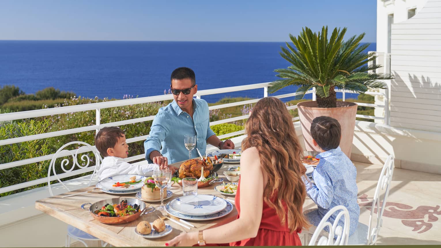A family dines on a terrace overlooking the vibrant blue waters