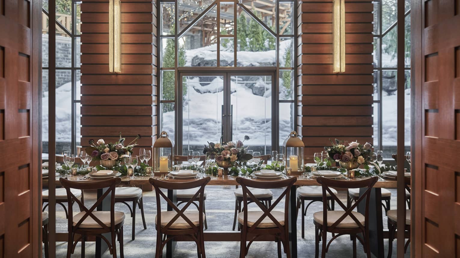 A dark brown table with several chairs overlooking a snowy mountain outside the window.