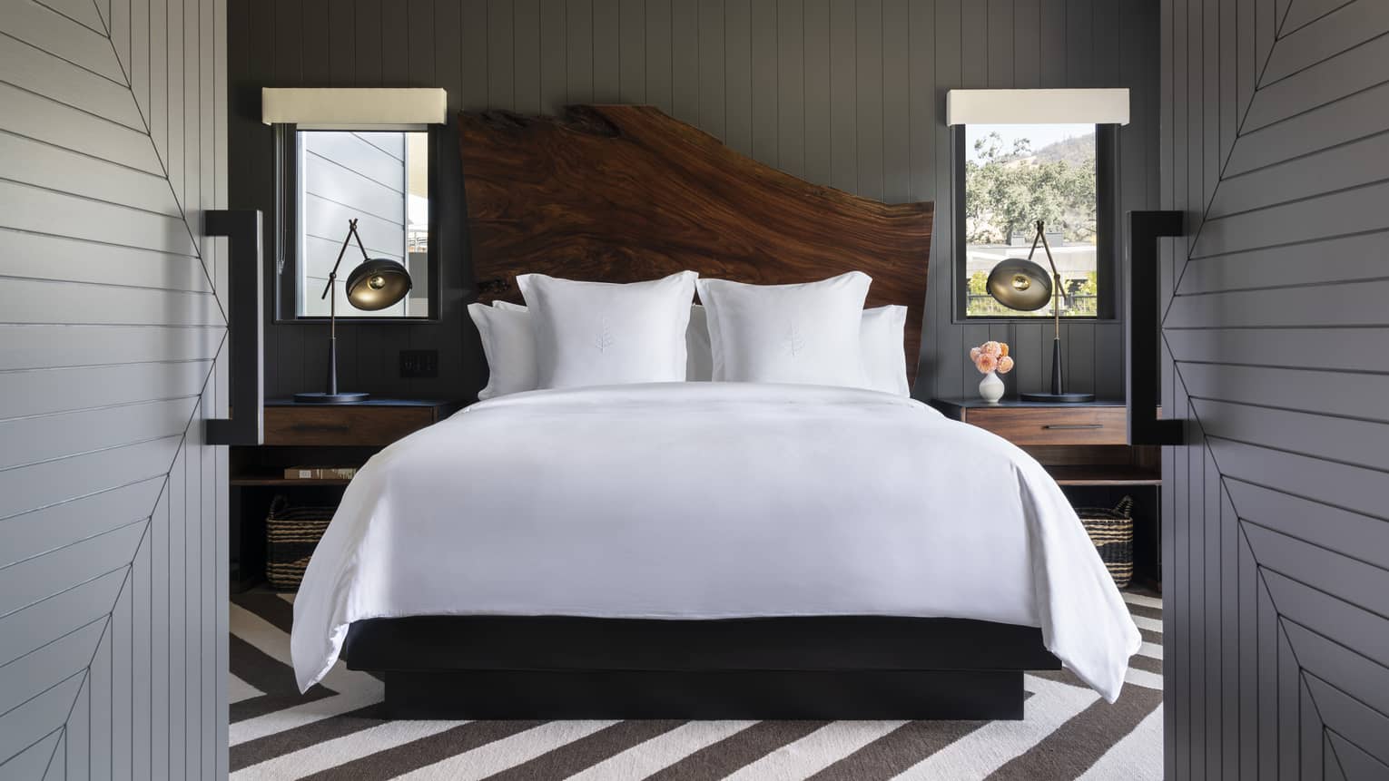 Luxury resort bedroom with a large white bed, wooden headboard and bedside tables with lamps in a dark-paneled room