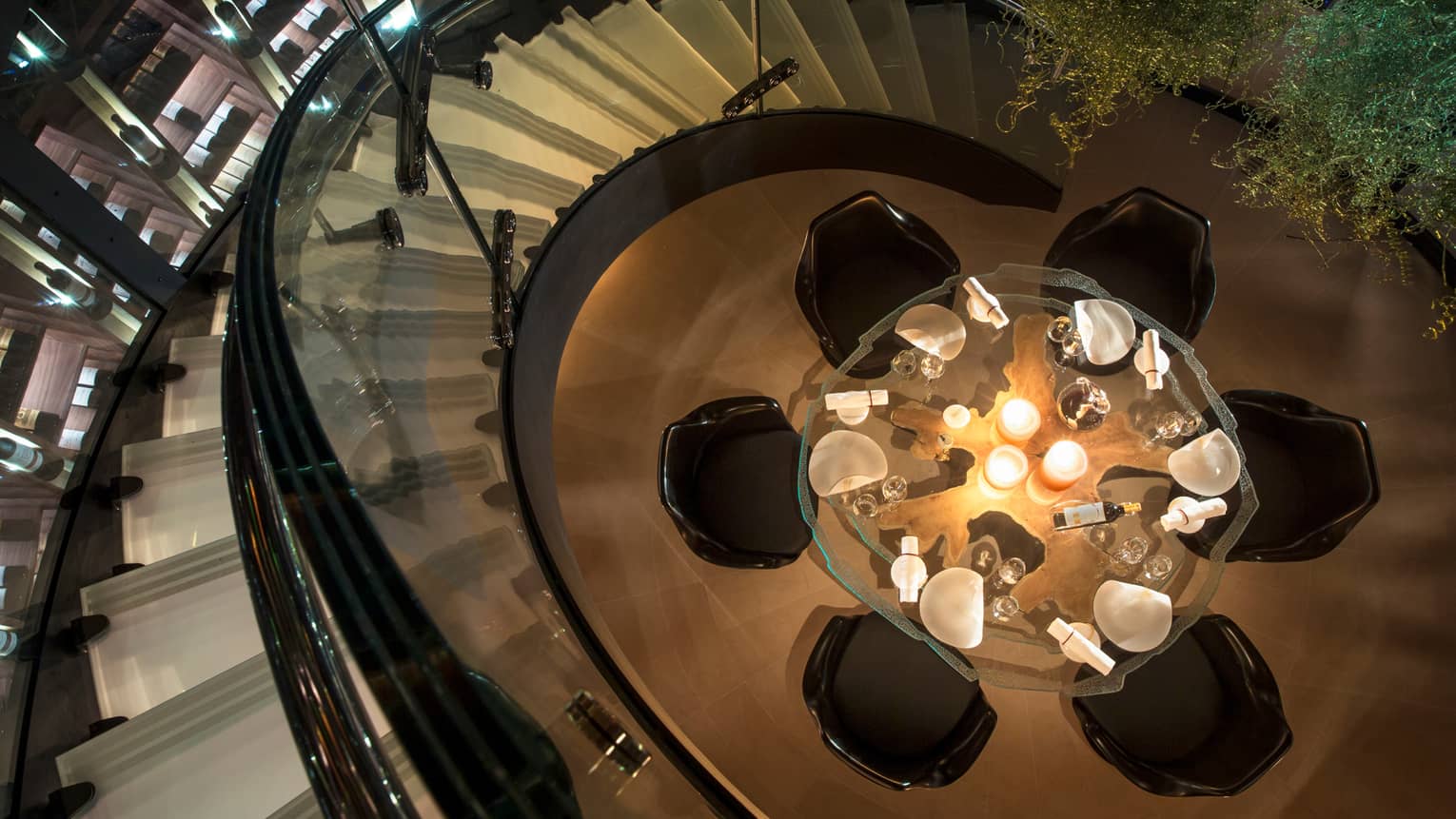 Aerial view of round glass candle-lit dining table, chairs from spiral staircase