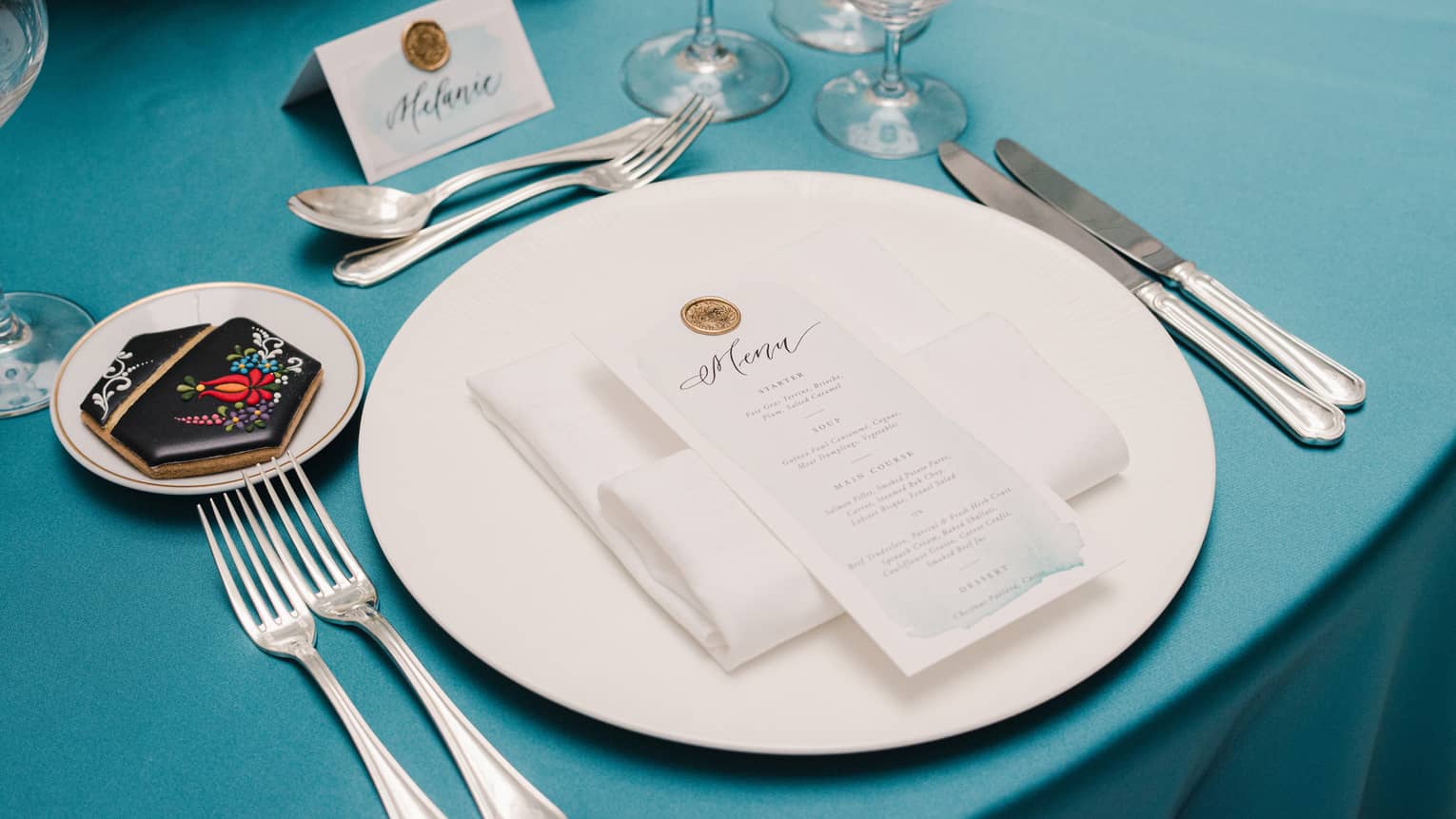 Formal white and silver table setting with place card on blue tablecloth