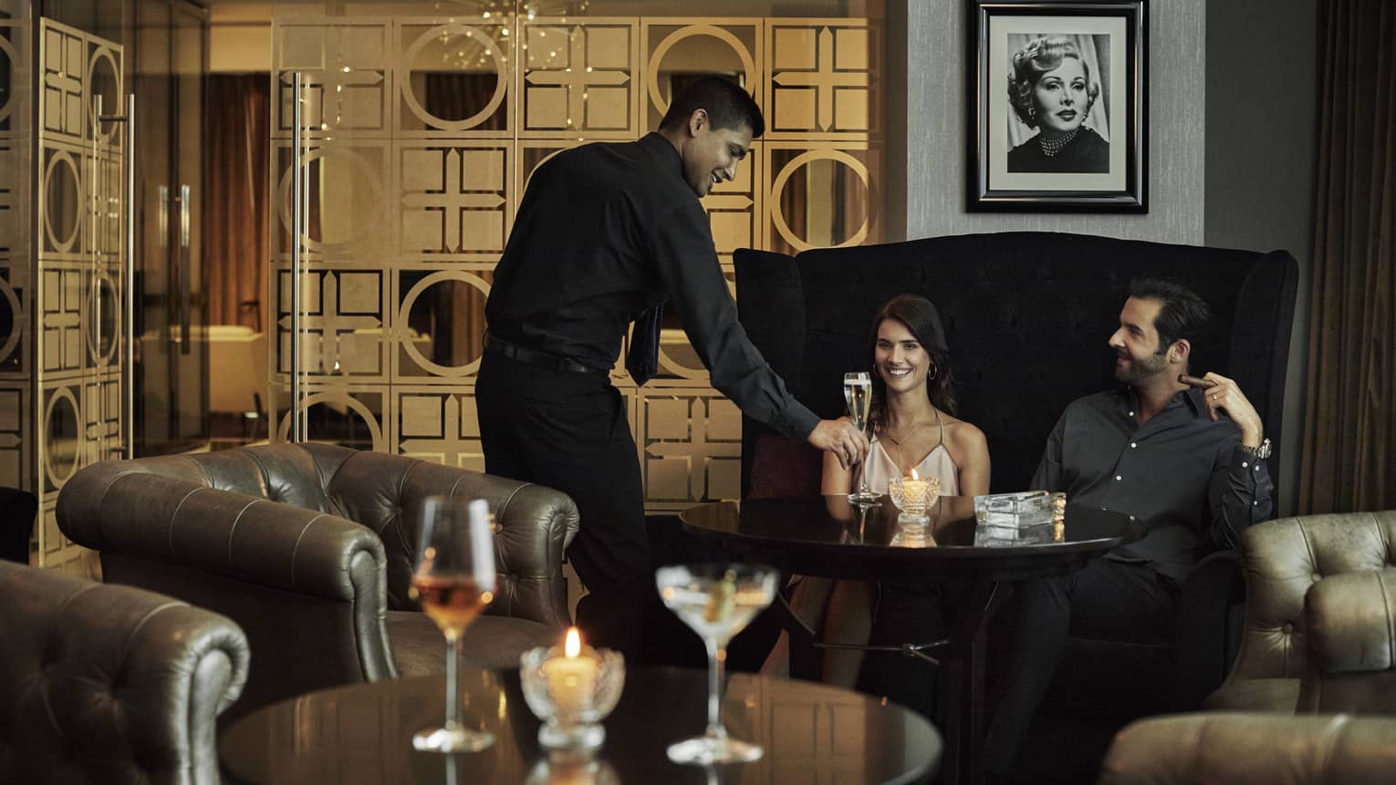 Zsa Zsa lounge staff places glass of Champagne on table in front of smiling couple