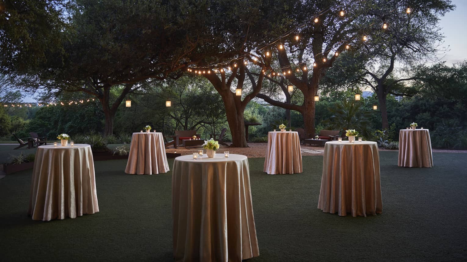 Small cocktail tables with silk linens across event lawn at night