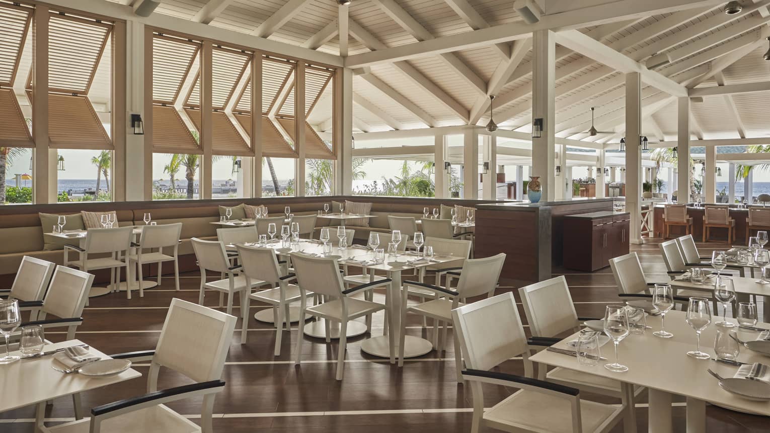 Indoor-outdoor restaurant with glass tables, white chairs, wooden beamed roof