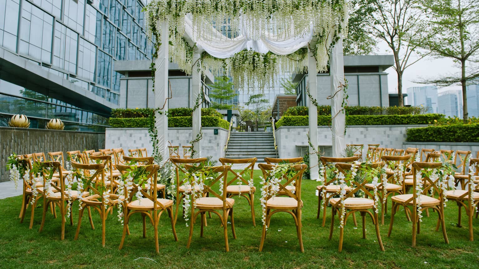 Wedding on event lawn, rows of chairs under large altar with white fabric, vines 